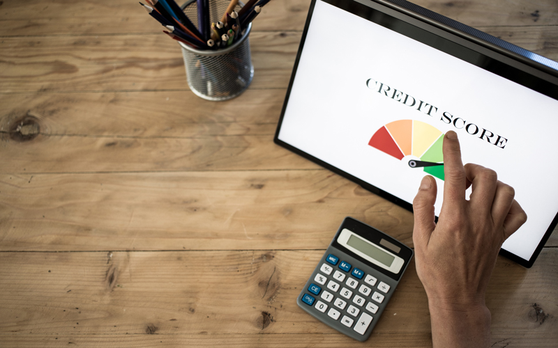 A person’s hand points at a digital screen displaying a credit score gauge, which ranges from red to green, with the needle leaning toward poor credit. The tablet sits on a rustic wooden desk alongside a calculator and a pencil holder filled with writing utensils, suggesting a workspace dedicated to financial review or planning. This image reflects the daily focus of credit repair professionals who rely on timely, compliant communication with clients, lenders, and credit bureaus. Postalocity’s secure mailing platform supports this industry with tools for sending dispute letters, compliance notices, and client updates—streamlining delivery while maintaining accuracy and confidentiality.
