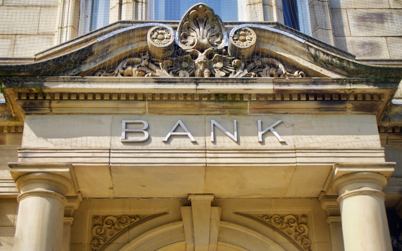 A classical stone bank building is shown in close-up, featuring ornate architectural details and large, carved columns. Above the entrance, the word “BANK” is prominently engraved in clean, modern lettering, symbolizing trust, tradition, and institutional authority. This image represents the financial sector—banks, credit unions, and lenders—that rely on Postalocity for secure, high-volume mailings such as account statements, certified notices, and compliance documents. The visual reinforces the need for accuracy, confidentiality, and timeliness in financial communication, all of which Postalocity delivers through its adaptable, secure mailing platform tailored to industry-specific demands.