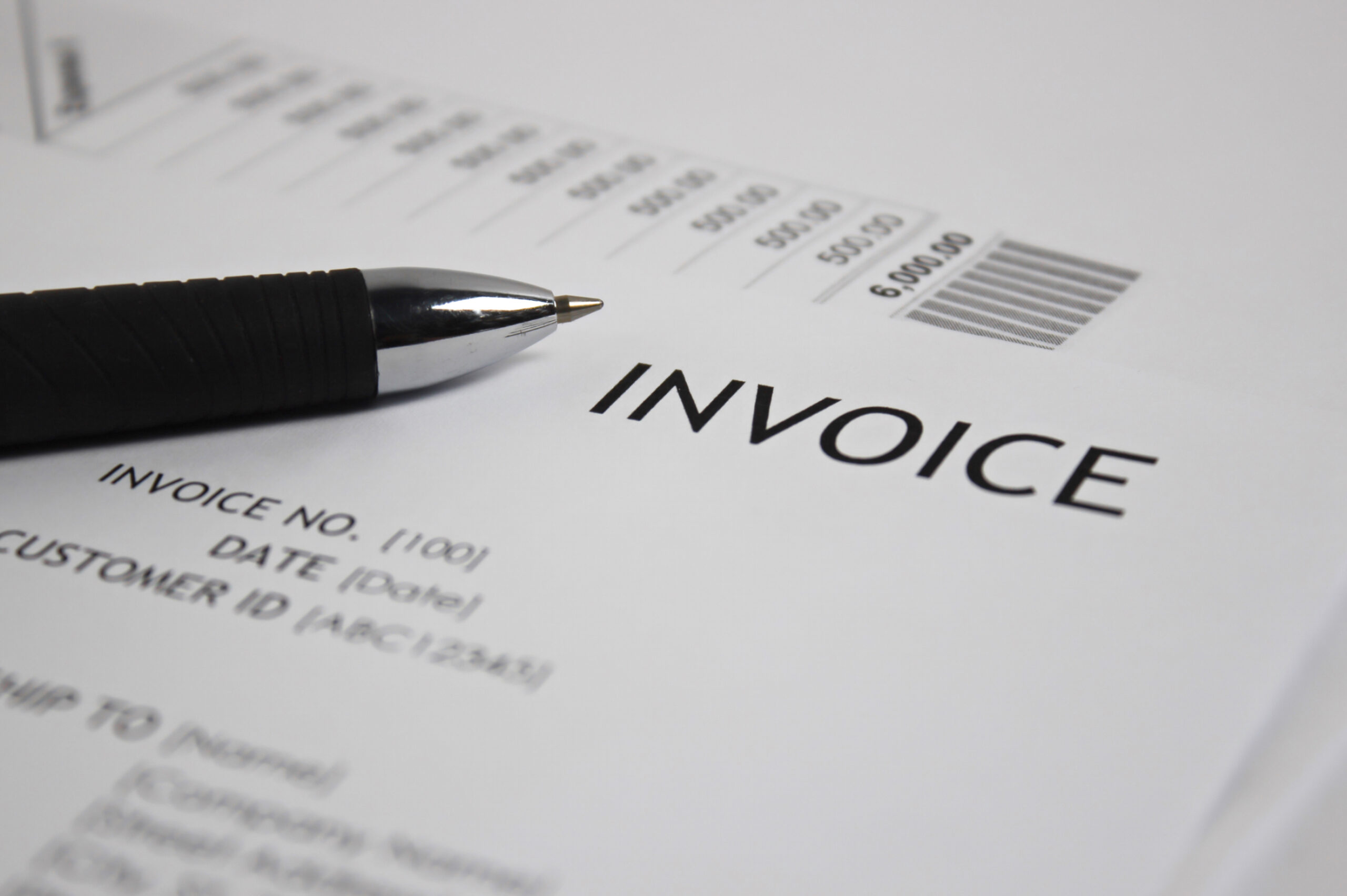 A close-up image of a printed invoice shows the bold word “INVOICE” prominently displayed at the top, along with visible details such as invoice number, date, customer ID, and a barcode. A black and chrome pen lies diagonally across the document, ready for use. The image conveys professionalism and precision, illustrating the kind of documents businesses and municipalities regularly send. It represents Postalocity’s reliable invoice mailing service, which offers same-day processing, advanced tracking capabilities, and a streamlined workflow for sending billing statements with accuracy, speed, and ease.