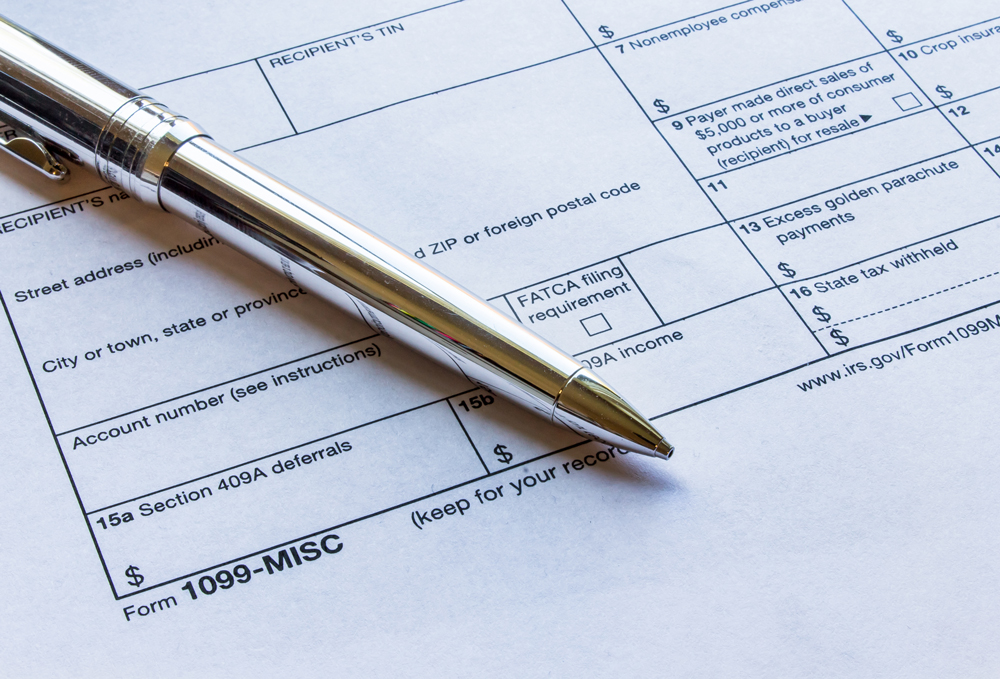 A close-up of a completed IRS Form 1099-MISC rests on a flat surface, with a sleek silver pen placed diagonally across the paper. The form includes labeled fields such as recipient information, account numbers, income sections, and FATCA filing requirements, clearly reflecting the structured nature of tax reporting. This visual represents the importance of secure, compliant document handling. It emphasizes Postalocity’s tax mailing service, which allows businesses to send 1099s, W-2s, and other official IRS tax forms safely and efficiently online—ensuring compliance while protecting sensitive financial information.